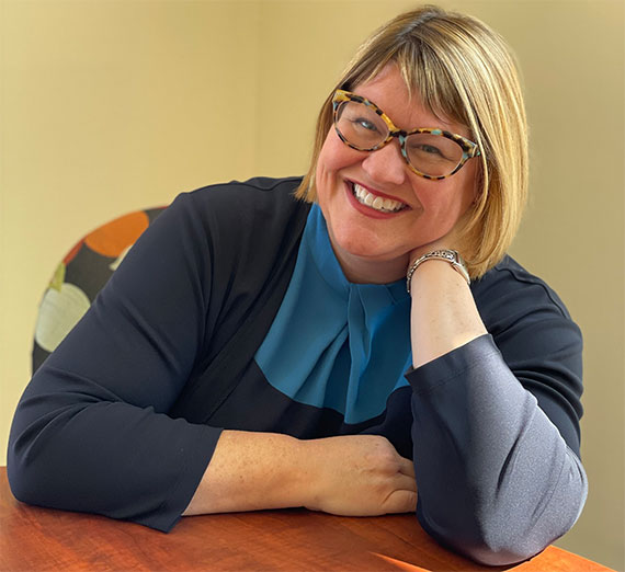 A group of five people stand together in a brightly lit hospital hallway, smiling at the camera. Two wear stethoscopes and medical attire, one wears a Gonzaga University sweatshirt, and others are dressed in casual or professional clothing, representing a mix of students and healthcare professionals.